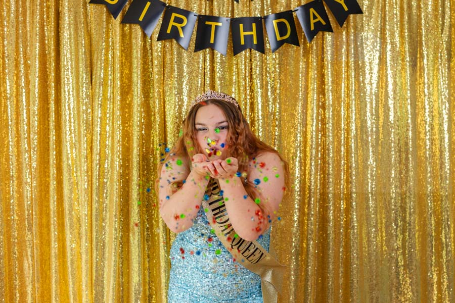 High school student blowing colorful confetti in front of a gold backdrop and Happy Birthday banner