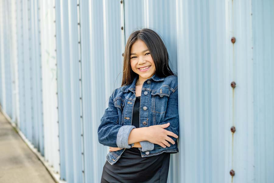A young asian girl leaning against a blue metal wall.